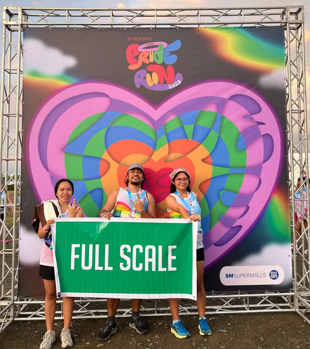 Three Full Scale employees holding a company banner at a public Pride Run event