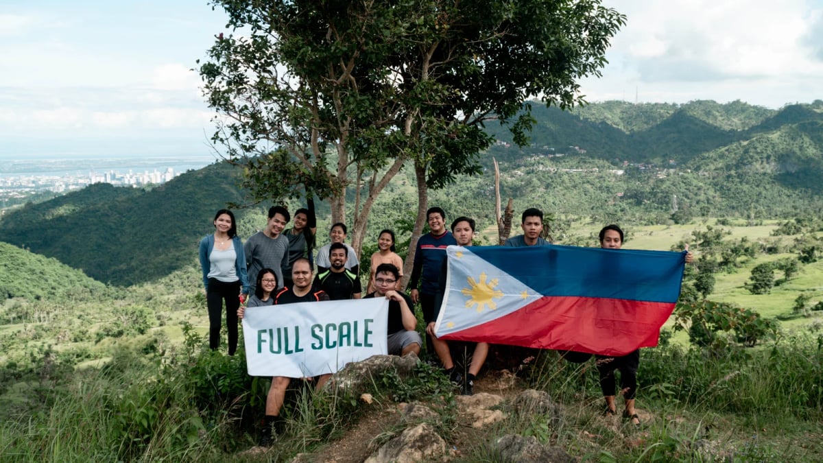 Full Scale employees holding a company banner and a Philippine flag at a mountain summit
