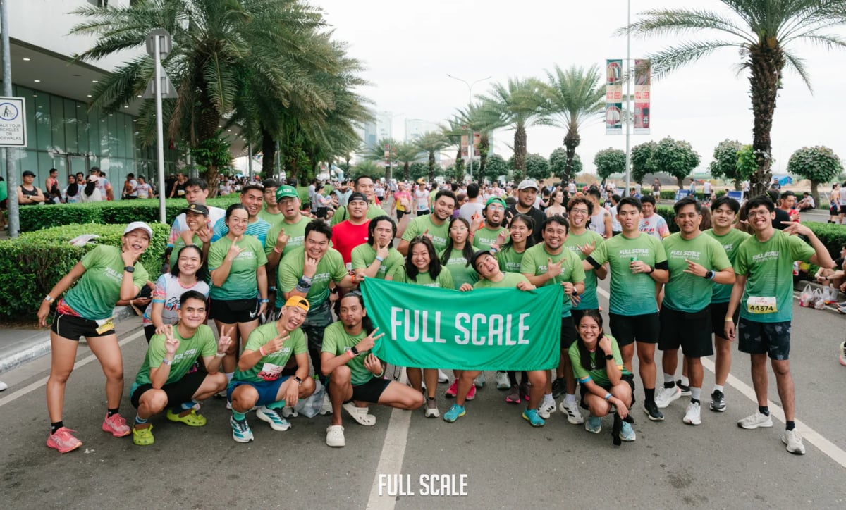 The Full Scale running club holding a company banner together at a public marathon