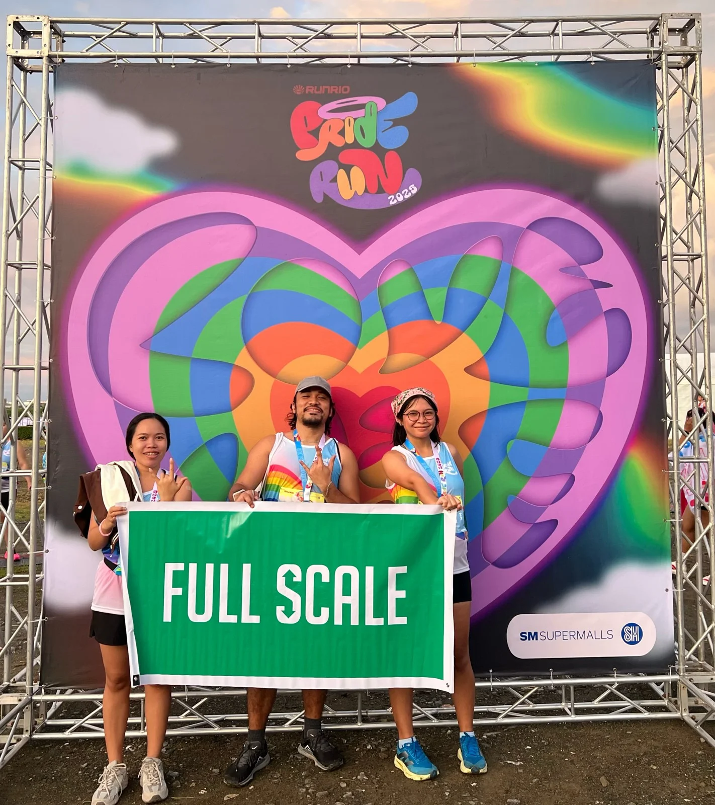 Three Full Scale employees holding a company banner at a public Pride Run event