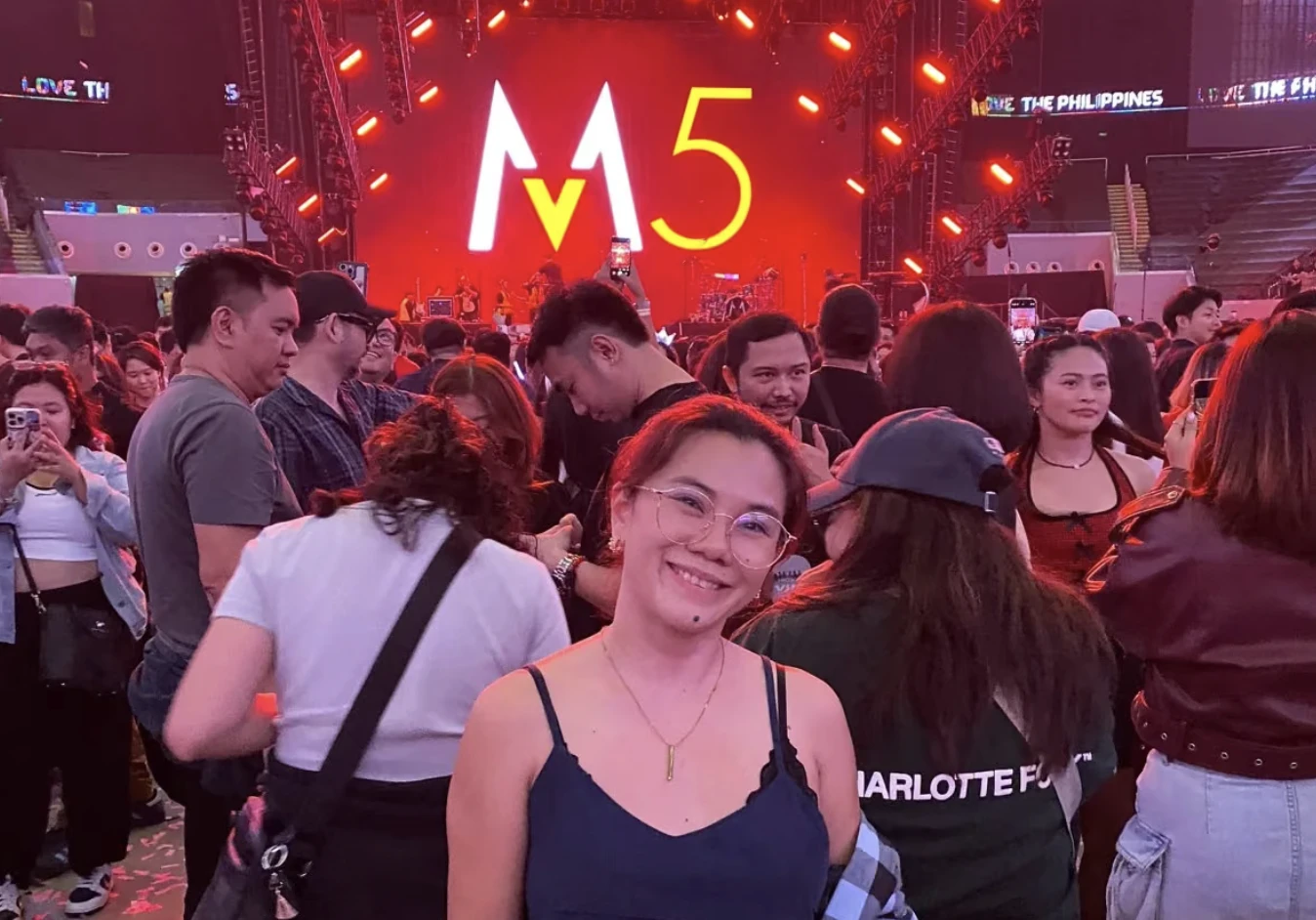 A Full Scale employee smiling at the Maroon 5 concert, the illuminated M5 stage screen behind her